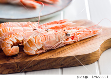 Scampi langoustine on cutting board on white table. Scampi langoustine on cutting board on white table. 129270291