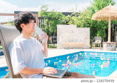 プールサイドのリクライニングチェアに座り水分補給する若いアジア人男性 プールサイドのリクライニングチェアに座り水分補給する若いアジア人男性 129270439