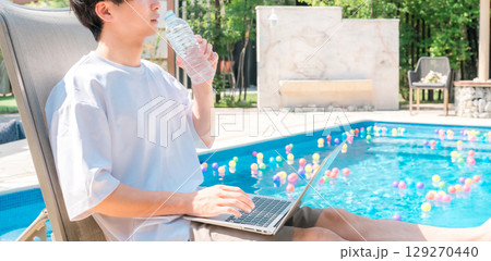 プールサイドのリクライニングチェアに座り水分補給する若いアジア人男性 プールサイドのリクライニングチェアに座り水分補給する若いアジア人男性 129270440