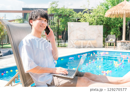 プールサイドのリクライニングチェアに座りスマホで通話する若いアジア人男性(予約,ルームサービス) プールサイドのリクライニングチェアに座りスマホで通話する若いアジア人男性(予約,ルームサービス) 129270577