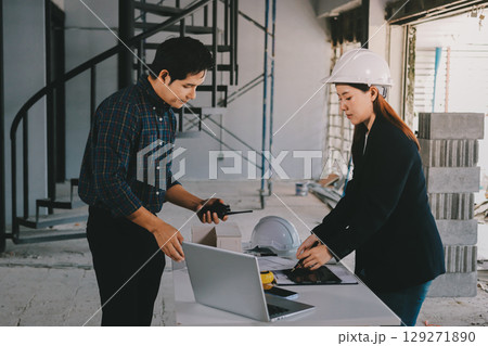 Construction manager and engineer dressed in orange work vests and hard helmets explore construction documentation on the building site near the steel frames 129271890