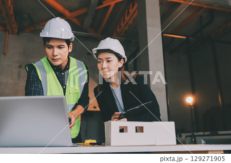 Construction manager and engineer dressed in orange work vests and hard helmets explore construction documentation on the building site near the steel frames 129271905