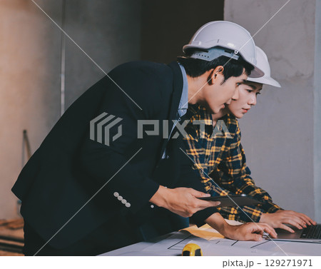 Construction manager and engineer dressed in orange work vests and hard helmets explore construction documentation on the building site near the steel frames Construction manager and engineer dressed in orange work vests and hard helmets explore construction documentation on the building site near the steel frames 129271971