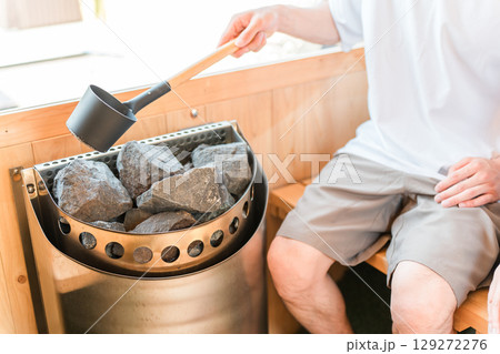 サウナに入ってロウリュする若いアジア人男性の手元 129272276