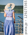 Woman with brown long hair and straw hat in summer dress walking near a lake 129273365