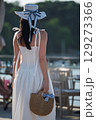 Woman with brown long hair and straw hat and bag in summer dress walking near a lake 129273366