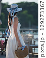 Woman with brown long hair and straw hat and bag in summer dress walking near a lake 129273367