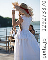 Woman with brown long hair and straw hat in summer dress walking near a lake 129273370
