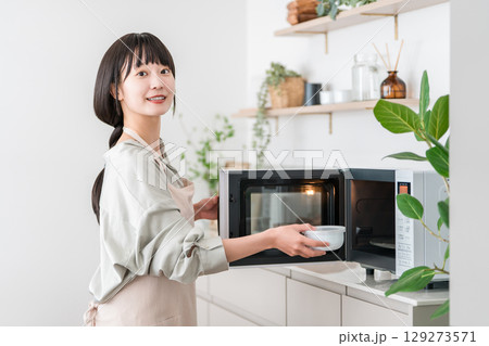 キッチンで電子レンジを使う女性(オーブンレンジ,温める) キッチンで電子レンジを使う女性(オーブンレンジ,温める) 129273571