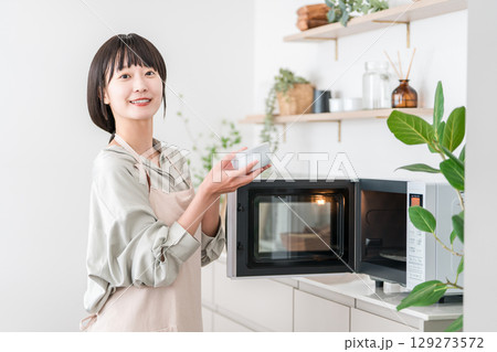 キッチンで電子レンジを使う女性（オーブンレンジ,温める) 129273572
