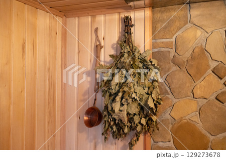 Oak leaves and ladle hanging in rustic wooden sauna interior 129273678