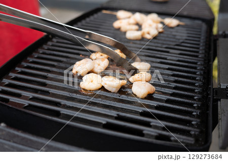 Grilled shrimp being cooked on barbecue grill with tongs 129273684
