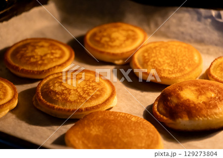 Warm golden-brown pancakes freshly baked in the oven, resting on parchment paper, offering a comforting homemade breakfast or delightful sweet dessert 129273804