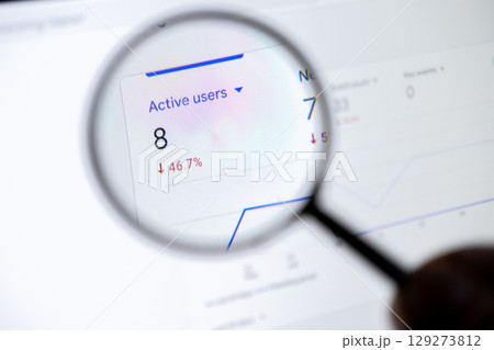 Magnifying glass examining a digital analytics dashboard displaying Active users with a sharp 46.7% decline, highlighting performance issues 129273812
