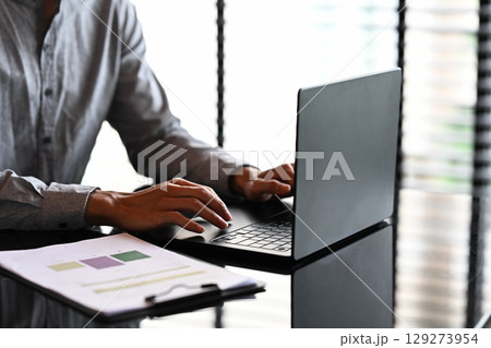 Close up of businessman working on a laptop with financial reports on the desk Close up of businessman working on a laptop with financial reports on the desk 129273954
