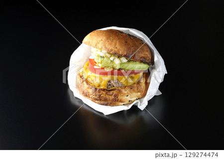 袋に包まれているチェダーチーズたっぷりのハンバーガーを黒背景で撮影 129274474