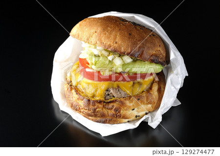 袋に包まれているチェダーチーズたっぷりのハンバーガーを黒背景で撮影 129274477