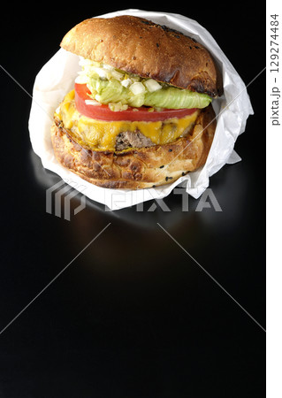 袋に包まれているチェダーチーズたっぷりのハンバーガーを黒背景で撮影 袋に包まれているチェダーチーズたっぷりのハンバーガーを黒背景で撮影 129274484