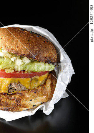 袋に包まれているチェダーチーズたっぷりのハンバーガーを黒背景で撮影 129274492