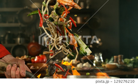 flying fresh ingredients in wok pan with whipping flames 129276210