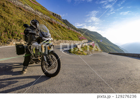 Motorcycle rider riding in Italian Alps during sunrise, dramatic sky. Travel and freedom, outdoor activities Motorcycle rider riding in Italian Alps during sunrise, dramatic sky. Travel and freedom, outdoor activities 129276236