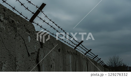 Concrete wall with barbed wire under gloomy sky symbolizes historical oppression 129276332