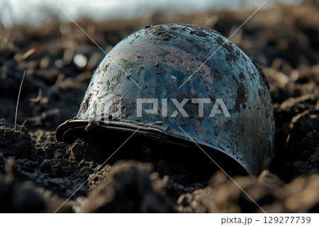 A mud-caked military helmet rests in the dark earth, evoking a sense of loss and the ravages of war 129277739