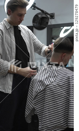 Professional barber carefully trimming customer's hair with electric clipper, providing a stylish and precise haircut in a modern barbershop environment 129278479