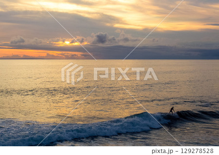 surfers catch a wave on the seashore at sunset 129278528
