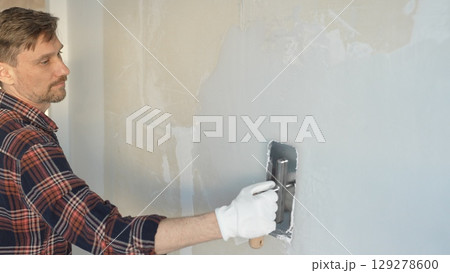 Male construction worker wearing gloves is carefully applying plaster to a wall using a hand tool, contributing to a home renovation or construction project Male construction worker wearing gloves is carefully applying plaster to a wall using a hand tool, contributing to a home renovation or construction project 129278600