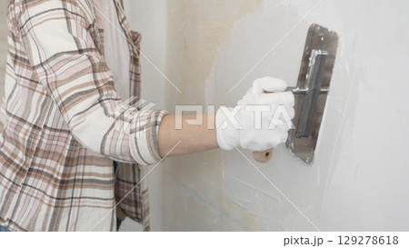 Unknown female construction worker wearing protective gloves applying plaster, smoothing wall surface during home renovation work 129278618