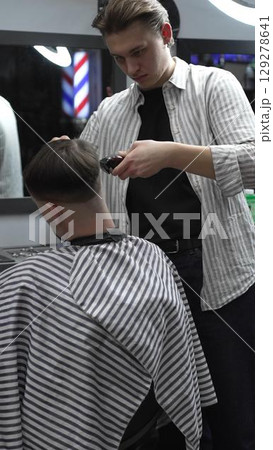 Professional barber carefully trimming customer's hair with electric clipper, providing a stylish and precise haircut in a modern barbershop environment Professional barber carefully trimming customer's hair with electric clipper, providing a stylish and precise haircut in a modern barbershop environment 129278641