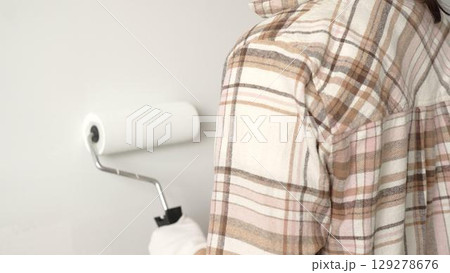 Painter's gloved hand gripping paint roller, spreading white paint across wall during home interior transformation with professional precision, close up view. Renovation concept Painter's gloved hand gripping paint roller, spreading white paint across wall during home interior transformation with professional precision, close up view. Renovation concept 129278676