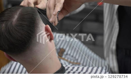 Professional barber cutting client's hair with scissors and comb, creating a stylish fade in a modern barbershop, providing a high quality grooming service Professional barber cutting client's hair with scissors and comb, creating a stylish fade in a modern barbershop, providing a high quality grooming service 129278734