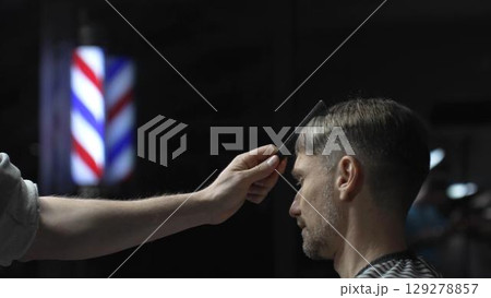Professional barber carefully checking customer's hair texture and head contours, preparing for precise haircut, vintage barbershop interior with iconic striped pole visible Professional barber carefully checking customer's hair texture and head contours, preparing for precise haircut, vintage barbershop interior with iconic striped pole visible 129278857