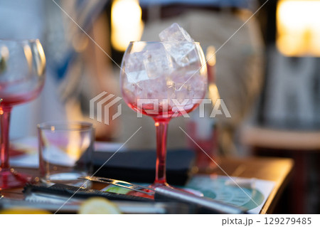 the bartender prepares an alcoholic cocktail by pouring ice cubes into a glass the bartender prepares an alcoholic cocktail by pouring ice cubes into a glass 129279485