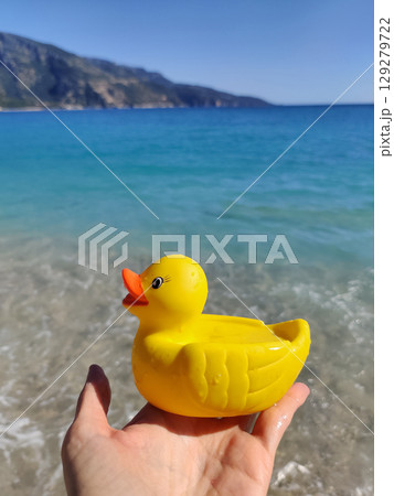 rubber toy yellow duck in hand with a view of the sea 129279722