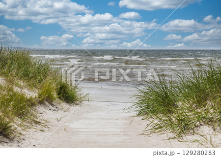Sandy dune path opening to sparkling Baltic Sea waves under bright summer sky 129280283