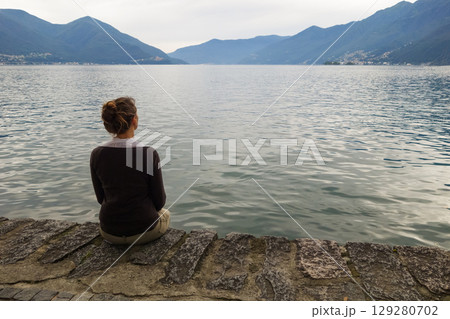 a beautiful girl sits on a stone pier looking at the sea a beautiful girl sits on a stone pier looking at the sea 129280702