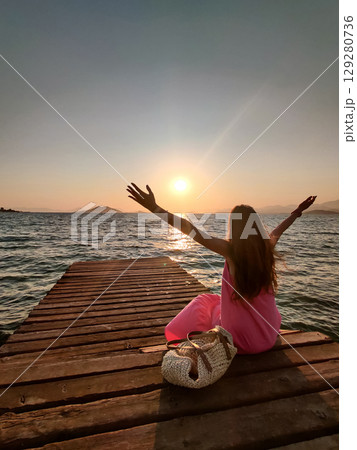 a beautiful girl sits on a sea pier at sunset 129280736