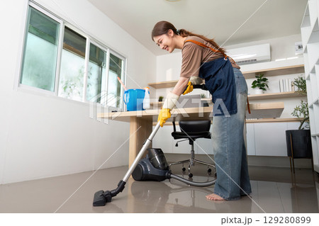 Home Cleaning. A young woman happily vacuuming her home office. Home Cleaning. A young woman happily vacuuming her home office. 129280899