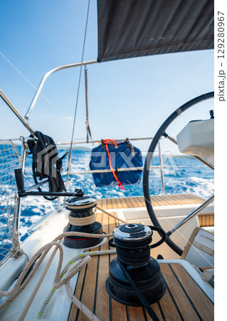 Cockpit of a sailing yacht with steering wheel, winches and ropes during navigation near Croatia. Sailing equipment, control and lifestyle at sea. 129280967