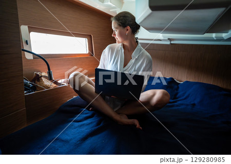 Young woman working with laptop and smartphone in the cabin of a sailing yacht near Croatia. Remote work, digital freedom and opportunity to live and work at sea. Young woman working with laptop and smartphone in the cabin of a sailing yacht near Croatia. Remote work, digital freedom and opportunity to live and work at sea. 129280985