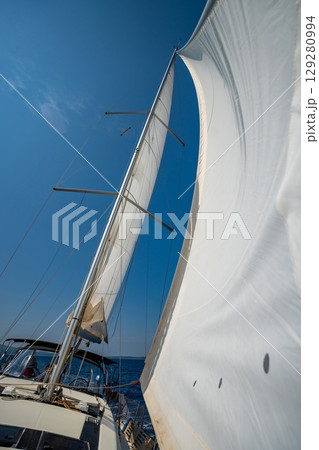White sails filled with wind, seen from the bow of a sailing yacht near Croatia. Freedom, clean energy, adventure and mindful travel on the open sea. White sails filled with wind, seen from the bow of a sailing yacht near Croatia. Freedom, clean energy, adventure and mindful travel on the open sea. 129280994