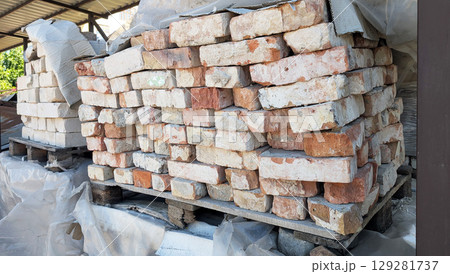 Piled bricks on pallets, wrapped in plastic for protection, displaying diverse colors and textures, ideal for construction and renovation projects 129281737