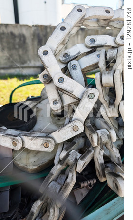 Close-up view of a heavy-duty metal chain resting on machinery, showcasing intricate links and textures, with green machinery components in the background, emphasizing industrial strength and durabili 129281738