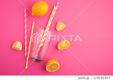 Preparing lemonade. Lemons, straws, and a glass on a vibrant pink background. Preparing lemonade. Lemons, straws, and a glass on a vibrant pink background. 129282407