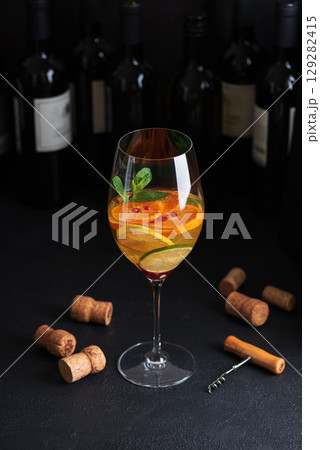 Sangria with citrus fruits and mint, corks and a corkscrew on a dark table with wine bottles. Sangria with citrus fruits and mint, corks and a corkscrew on a dark table with wine bottles. 129282415