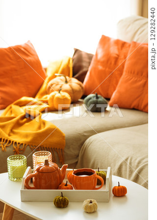 Autumnal living room decor with pumpkins, a teapot, tea cup, and cozy blankets. Autumnal living room decor with pumpkins, a teapot, tea cup, and cozy blankets. 129282440