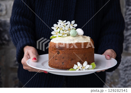 A woman holding a plate with a homemade Easter cake decorated with spring flowers and eggs. Horizontal. A woman holding a plate with a homemade Easter cake decorated with spring flowers and eggs. Horizontal. 129282541